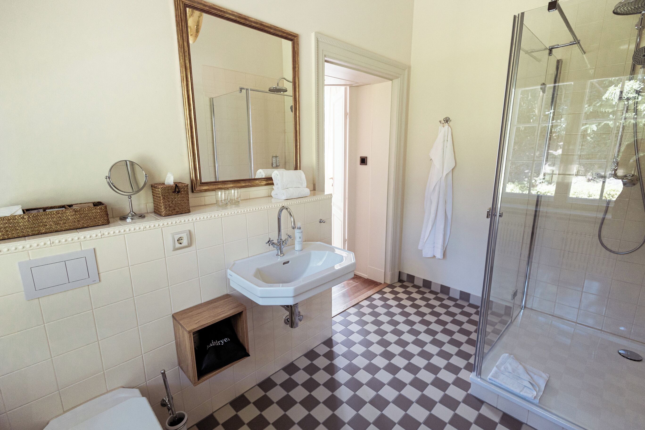 Une salle de bain avec un carrelage à motifs géométriques, un lavabo, un miroir, une douche et un porte-serviettes.