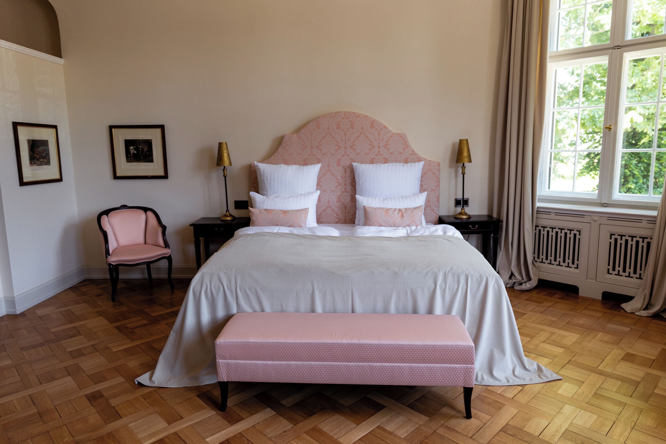A neatly arranged bedroom with a large bed, a chair, a bench, and framed pictures on the wall.
