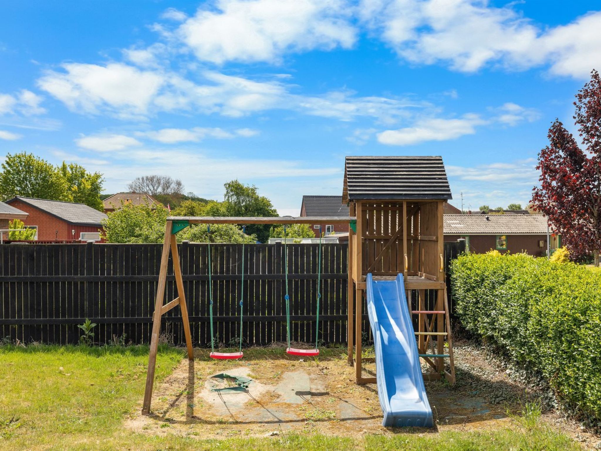 Ein Spielplatz im Garten mit Schaukel, Rutsche und einer kleinen Holz-Kletterkonstruktion.