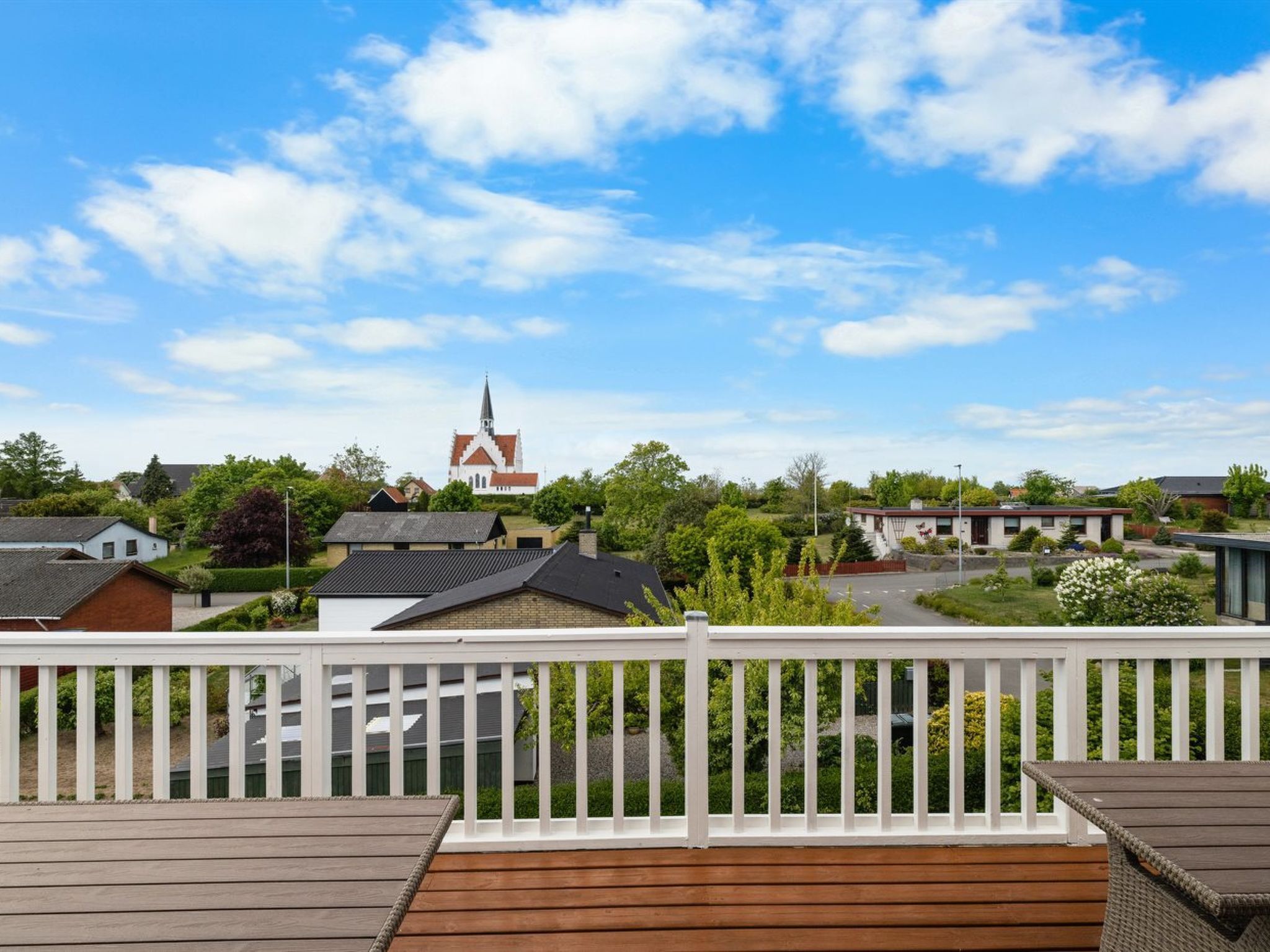 Ein Wohngebiet mit einer Kirche im Hintergrund, einer Holzterrasse im Vordergrund und Häusern mit unterschiedlichen Dachformen.