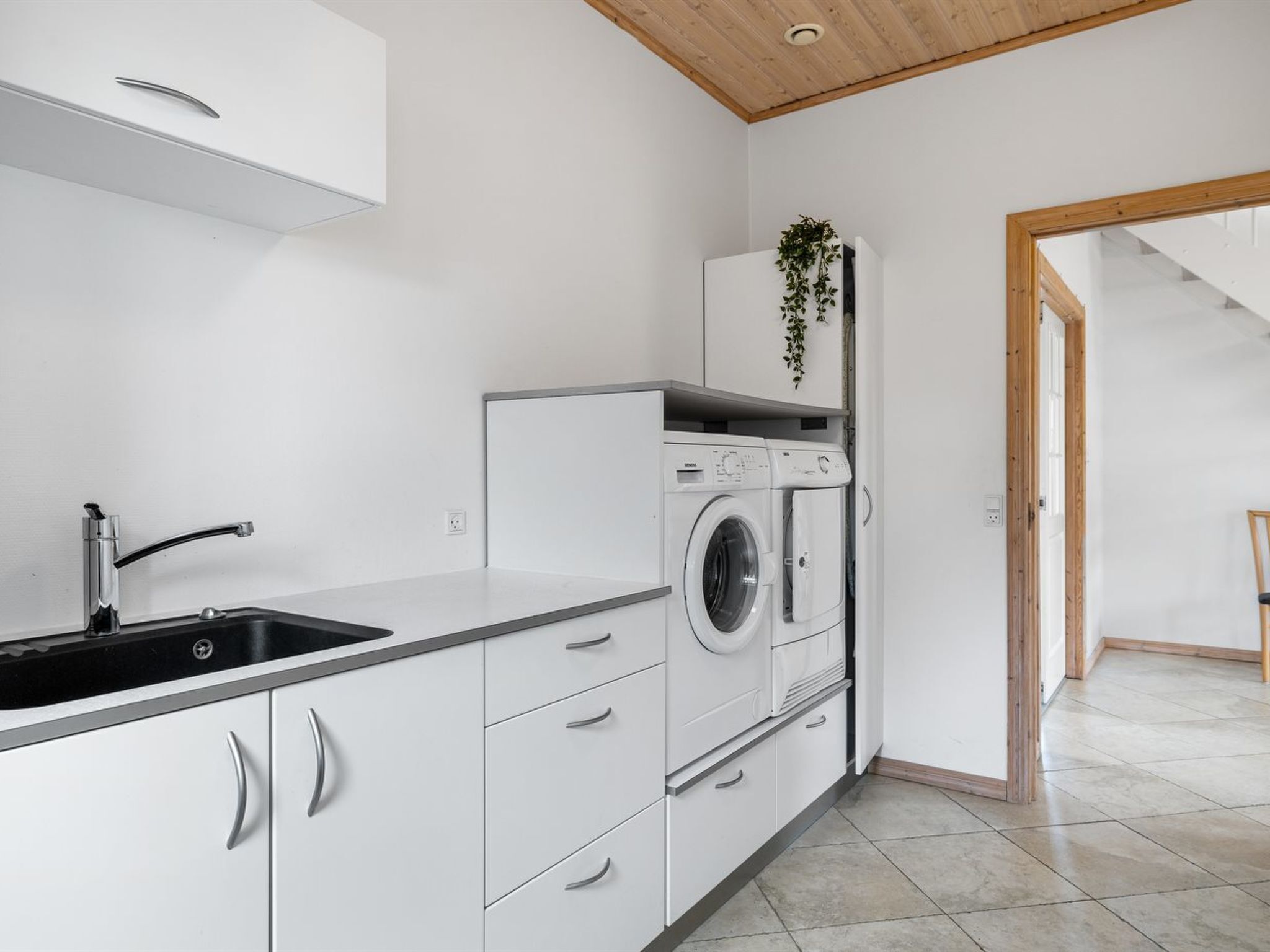 Une cuisine moderne avec des meubles blancs, un évier en acier inoxydable et un lave-linge encastré.