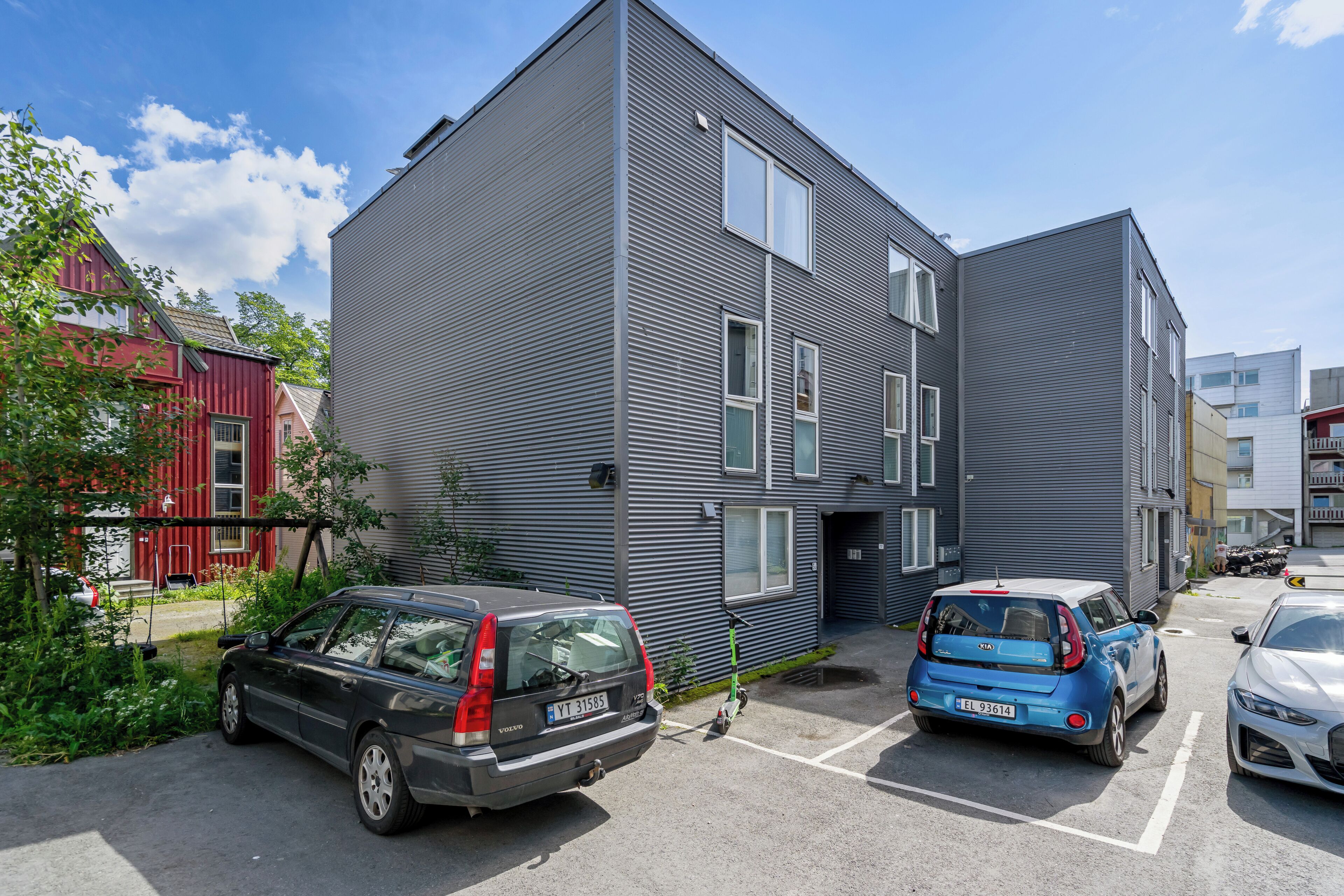 Een modern gebouw met een parkeerplaats, met een zwarte auto en een blauwe auto ervoor geparkeerd.
