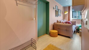 Un salon chaleureux avec une porte verte, un canapé, un petit pouf rond et une lampe sur pied.