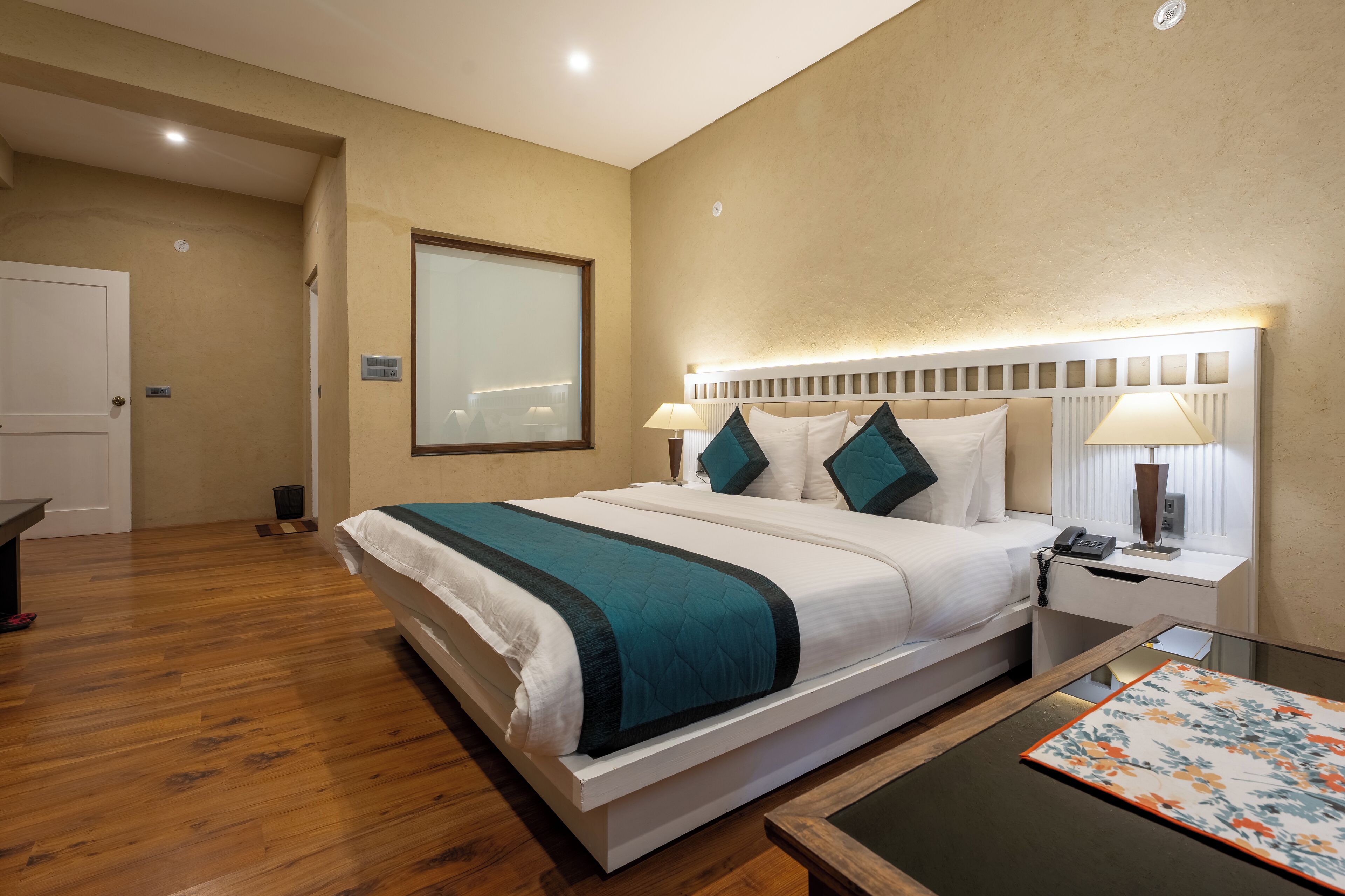 A modern hotel room with a large bed, bedside tables, a nightstand, and a view of the hallway.