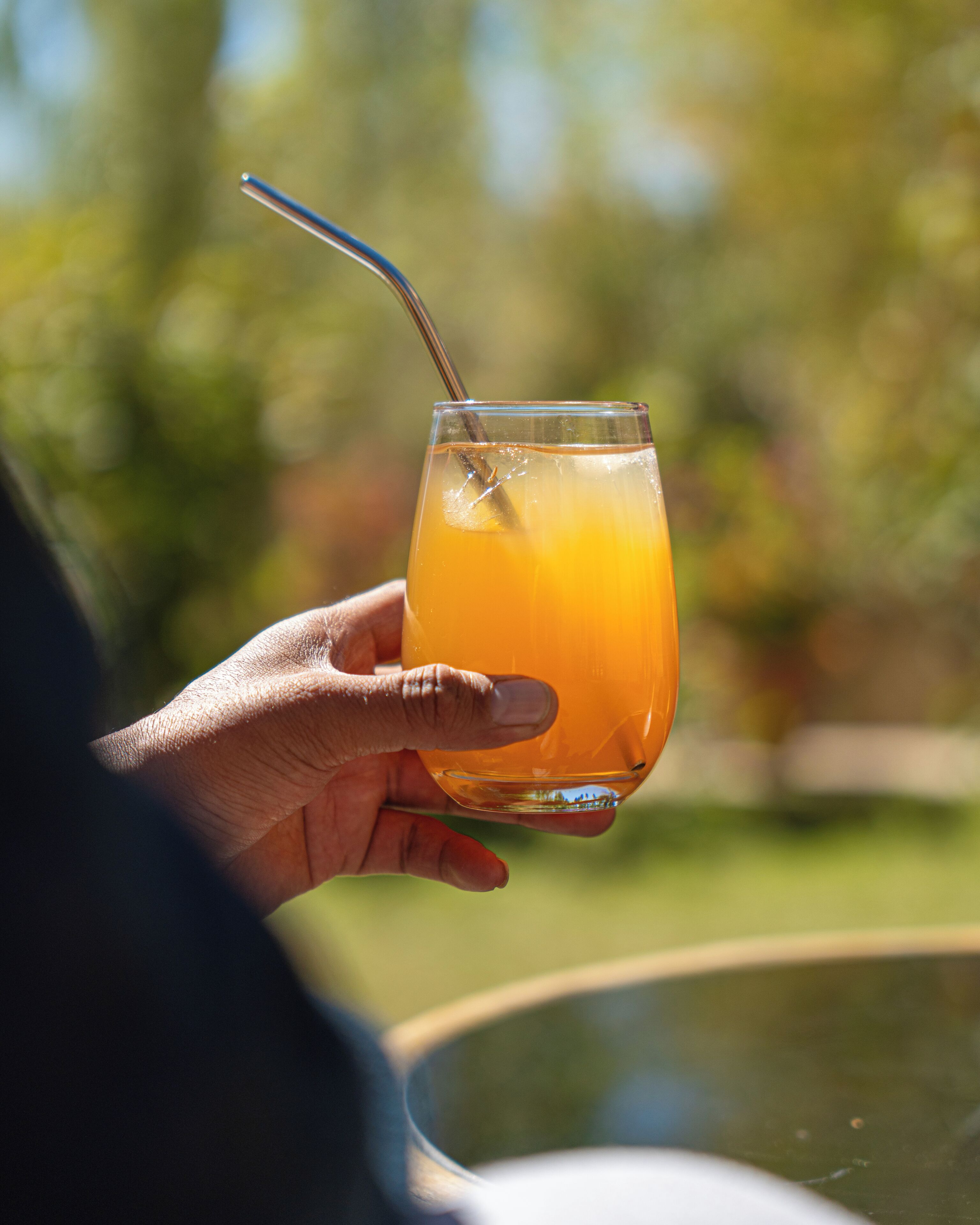 A hand holding a glass with a straw, containing a yellowish liquid, likely a beverage.