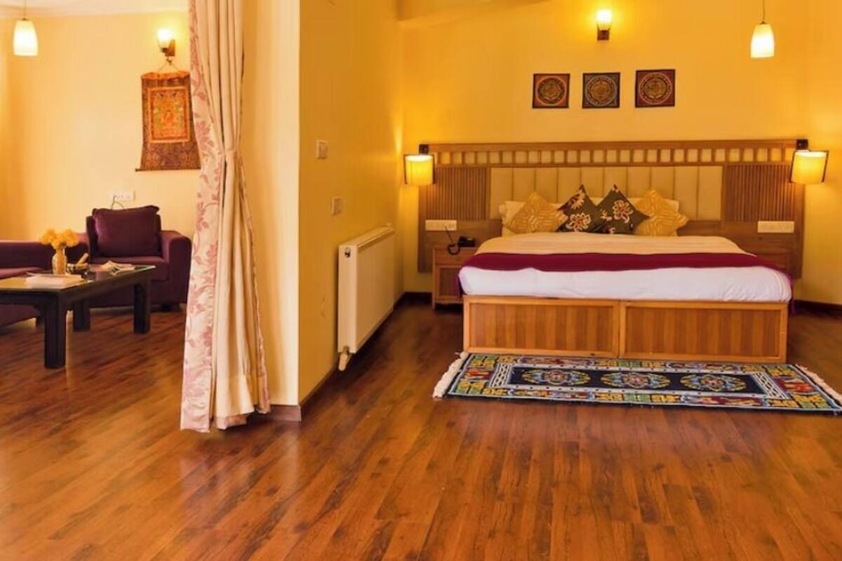 A hotel room with a wooden floor, a bed with a headboard, a sofa, a coffee table, and a patterned rug.