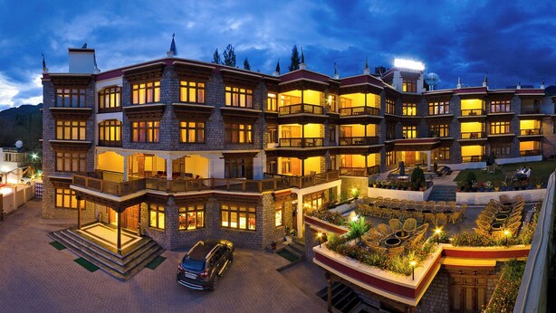 Un hotel de varios pisos con un patio, asientos al aire libre y un coche estacionado frente.