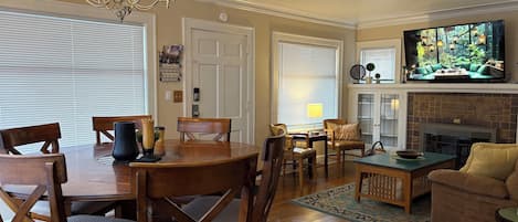 A dining area with a wooden table and chairs, a chandelier, and a television in the background.