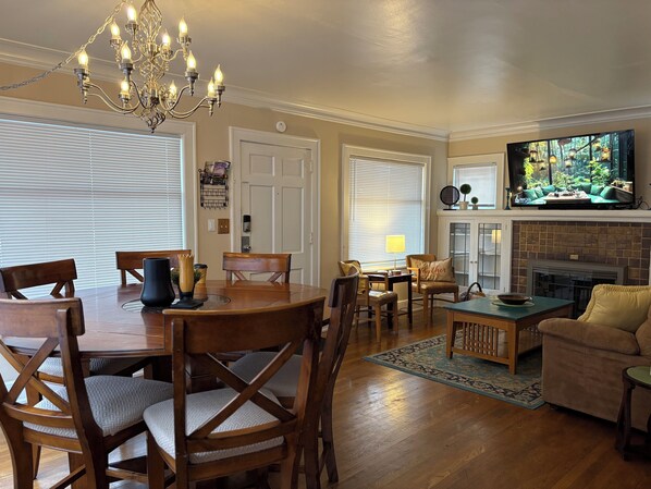 A dining area with a wooden table and chairs, a chandelier, and a television in the background. - Spacious 4-bedroom house in awesome Seattle with WiFi, AC (Seattle)