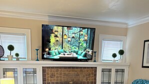 Una sala de estar con chimenea, un televisor montado encima, una mesa de centro de madera, un sofá y un tapete estampado.