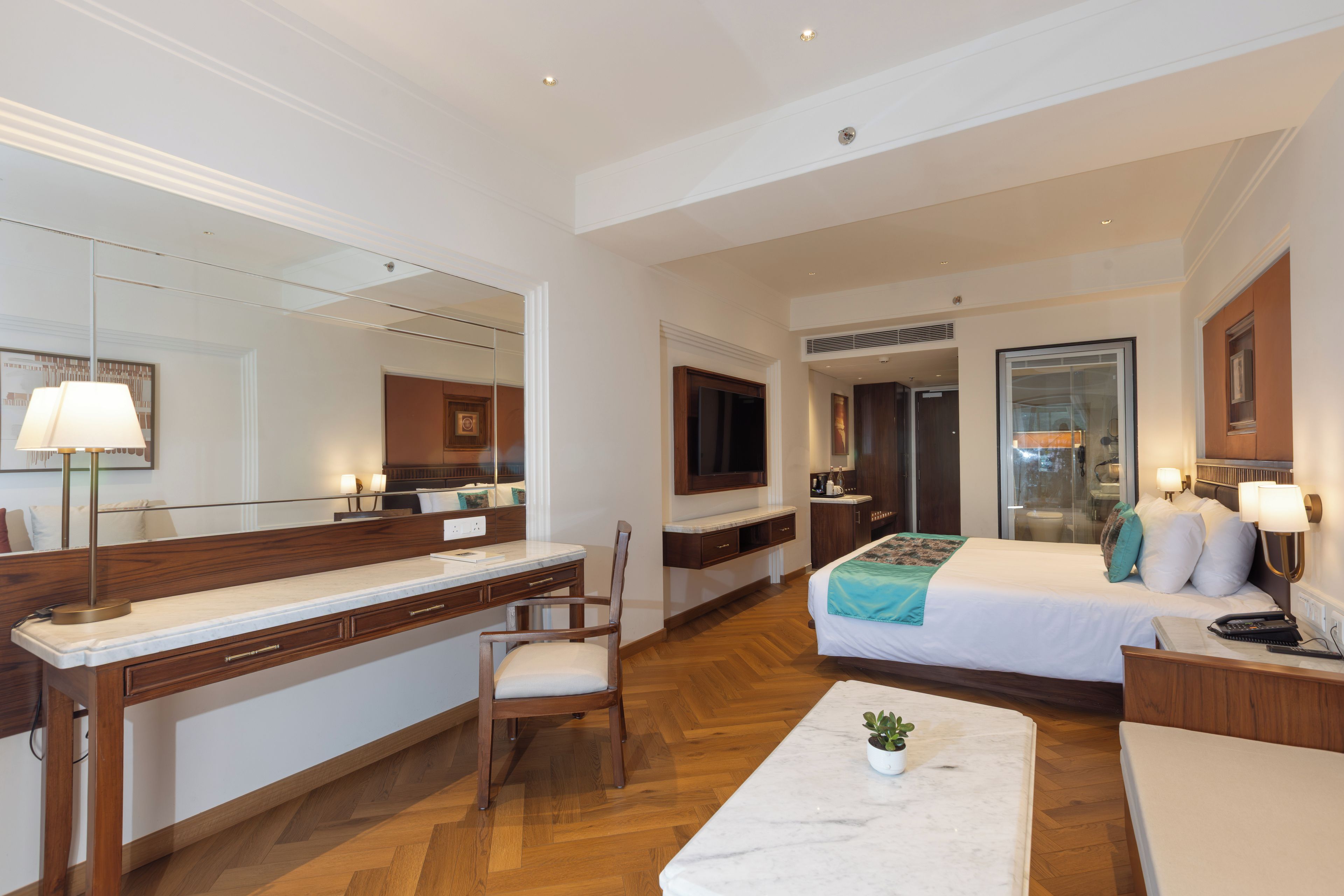 A hotel room with a large bed, a desk, a chair, a mirror, and a television.