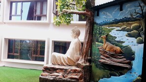 Una estatua de una figura sentada sobre un pedestal de roca, un árbol y un mural de un paisaje con un ciervo.