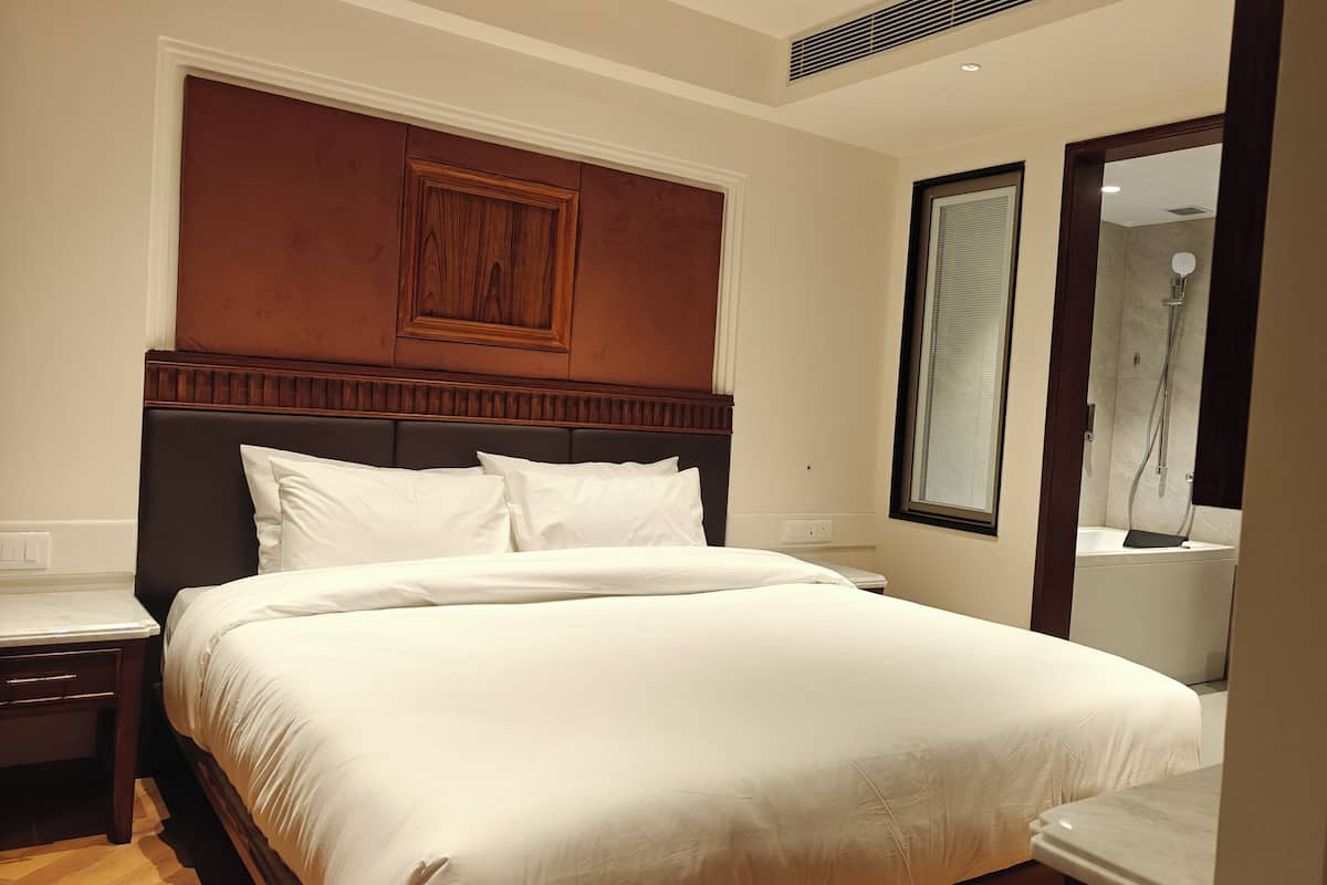 A hotel room with a large bed, a wooden headboard, a nightstand, a bathroom with a shower, and a mirror.