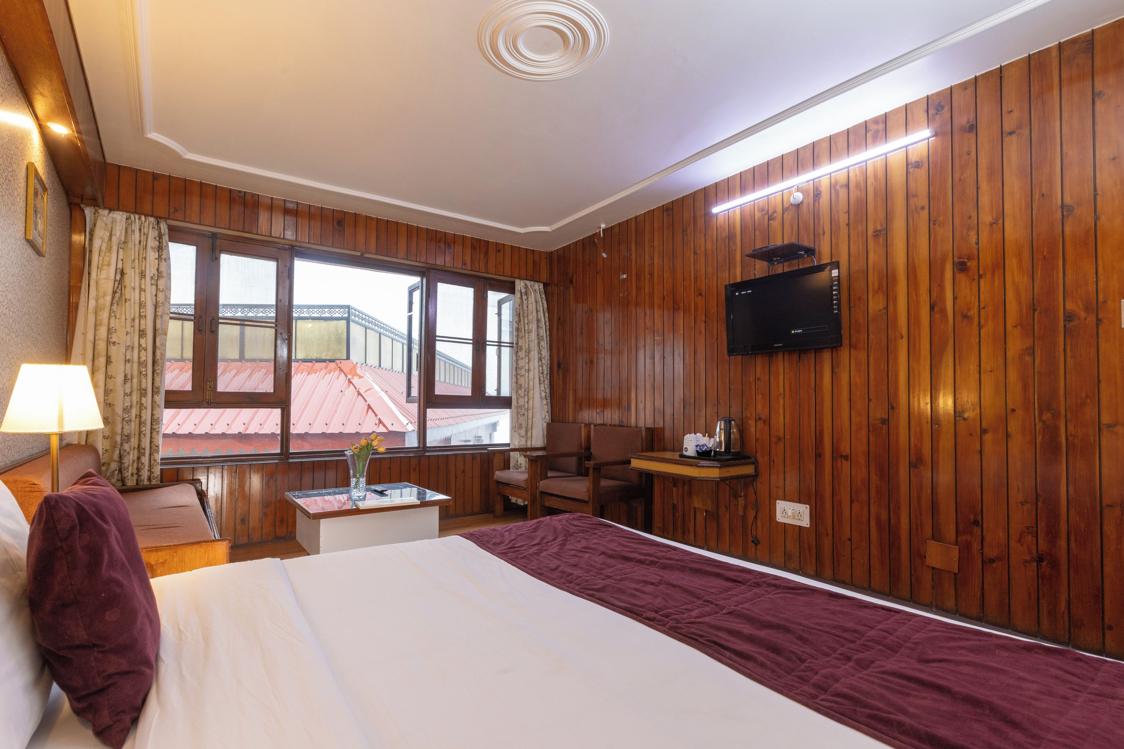 A hotel room with a bed, a desk, a chair, a TV, and a window with a view of buildings.