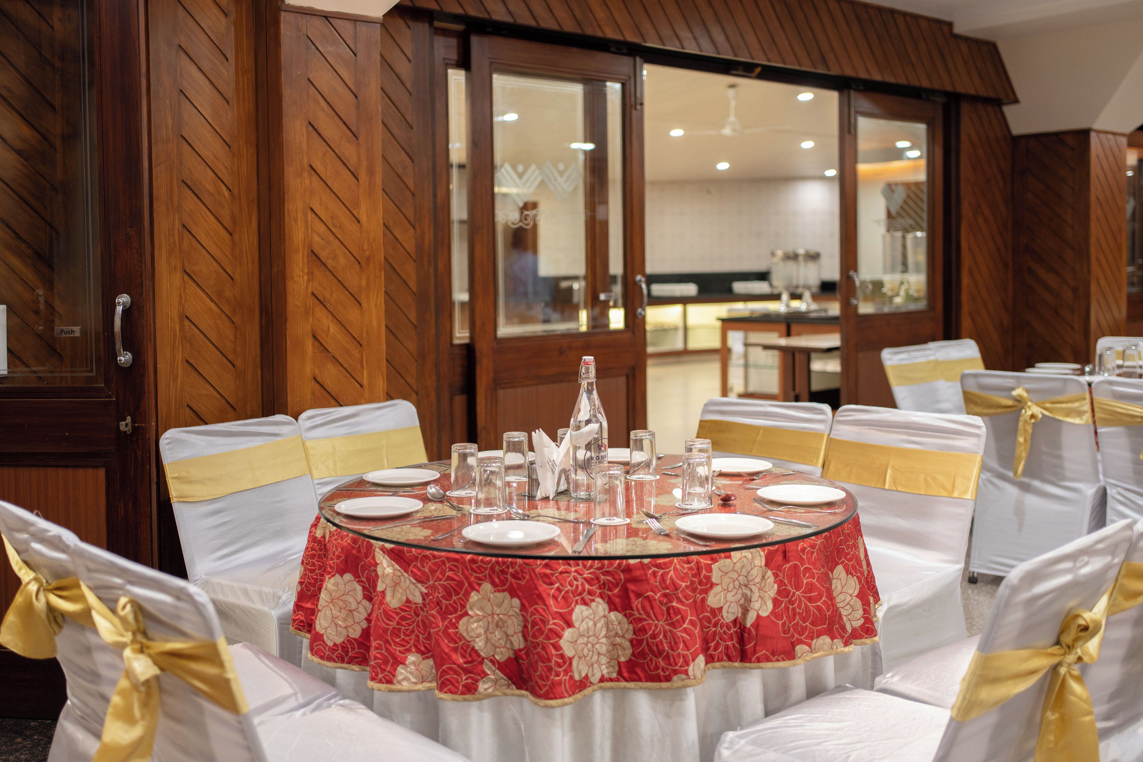 A dining area with round tables, white chairs with yellow sashes, and a red floral tablecloth.
