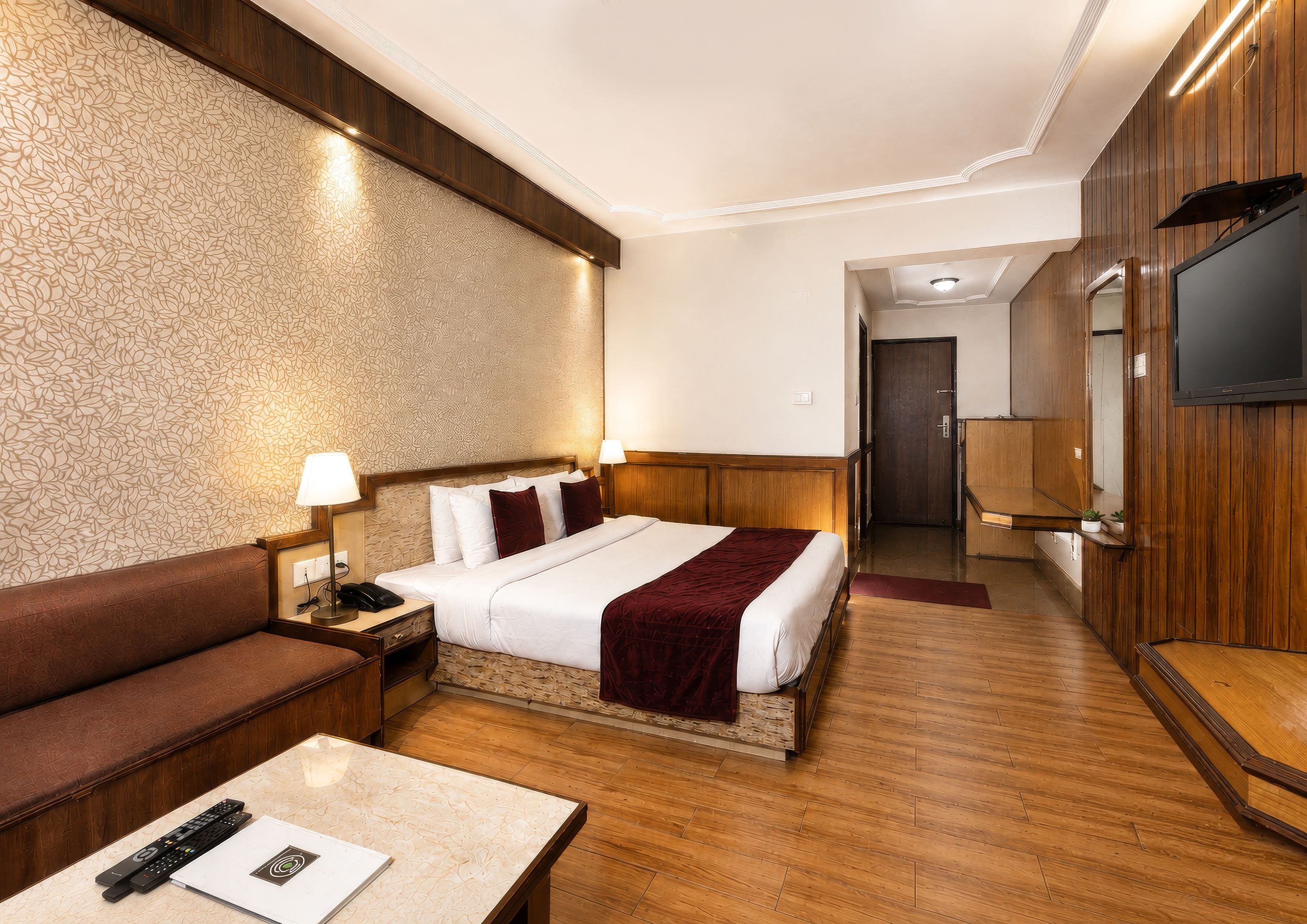A hotel room with a bed, a sofa, a TV, and a desk with a remote control.