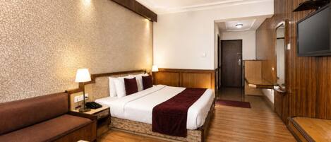 A hotel room with a bed, a sofa, a TV, and a desk with a remote control.
