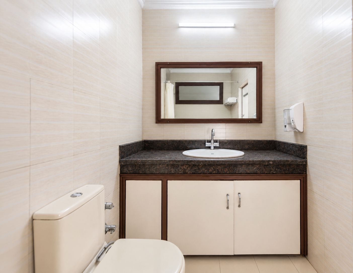 Ein Badezimmer mit einer weißen Toilette, einem Waschbecken mit dunkler Arbeitsplatte und einem Spiegel darüber.