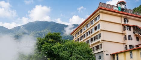 A multi-story building with a red roof, surrounded by lush greenery and mountains in the background.