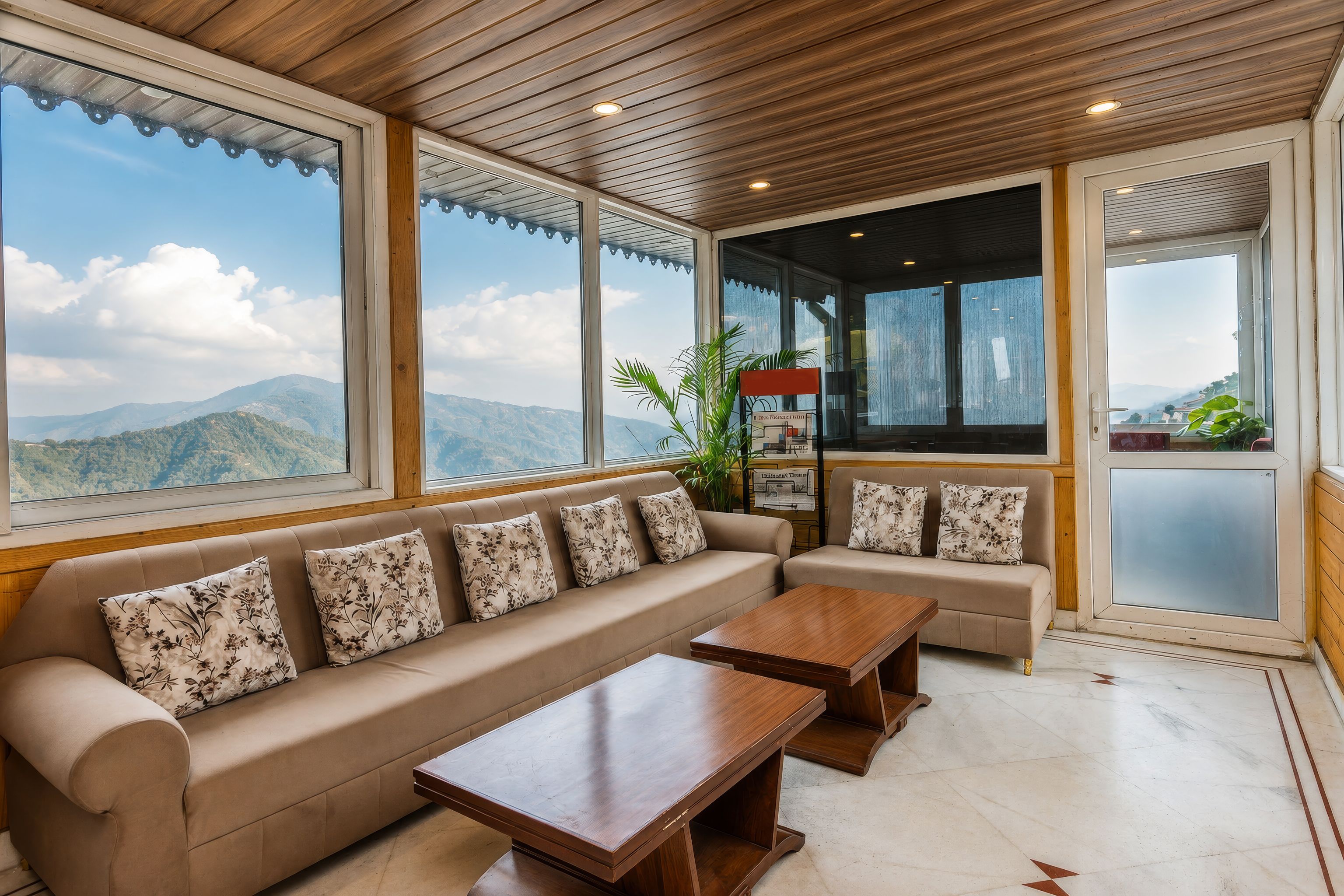 Amplia habitación con un sofá grande y una mesa de centro de madera, ventanas amplias con vistas a la montaña y techo de madera.