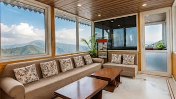 Amplia habitación con un sofá grande y una mesa de centro de madera, ventanas amplias con vistas a la montaña y techo de madera.