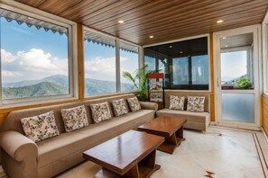 A spacious room with a large sofa and a wooden coffee table, large windows with a mountain view, and a wooden ceiling. - Hotel Vishnu Palace (Uttarakhand)