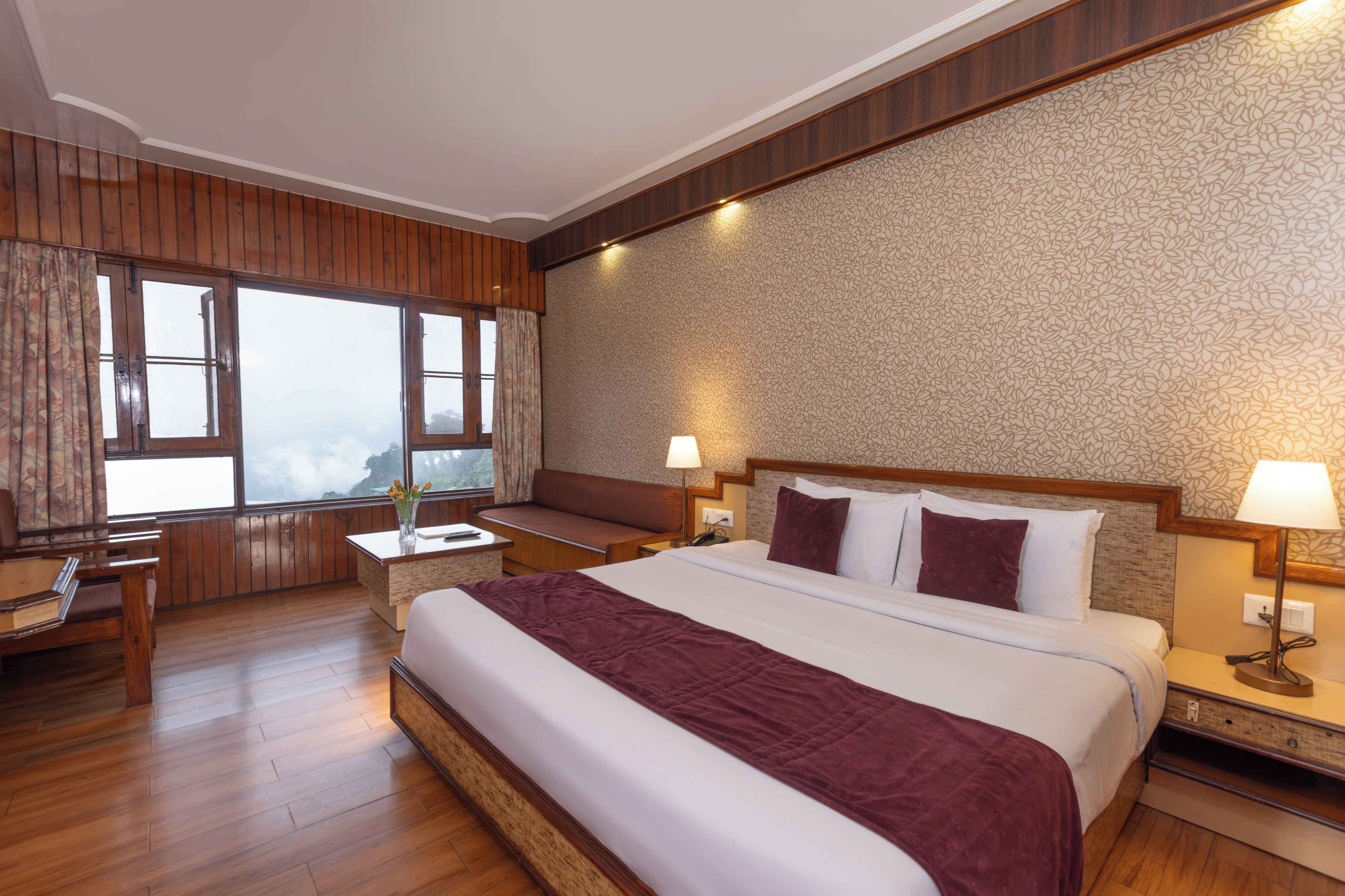 Quarto de hotel com uma cama grande, piso de madeira, escrivaninha e vista para o exterior.