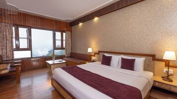 Quarto de hotel com uma cama grande, piso de madeira, escrivaninha e vista para o exterior.