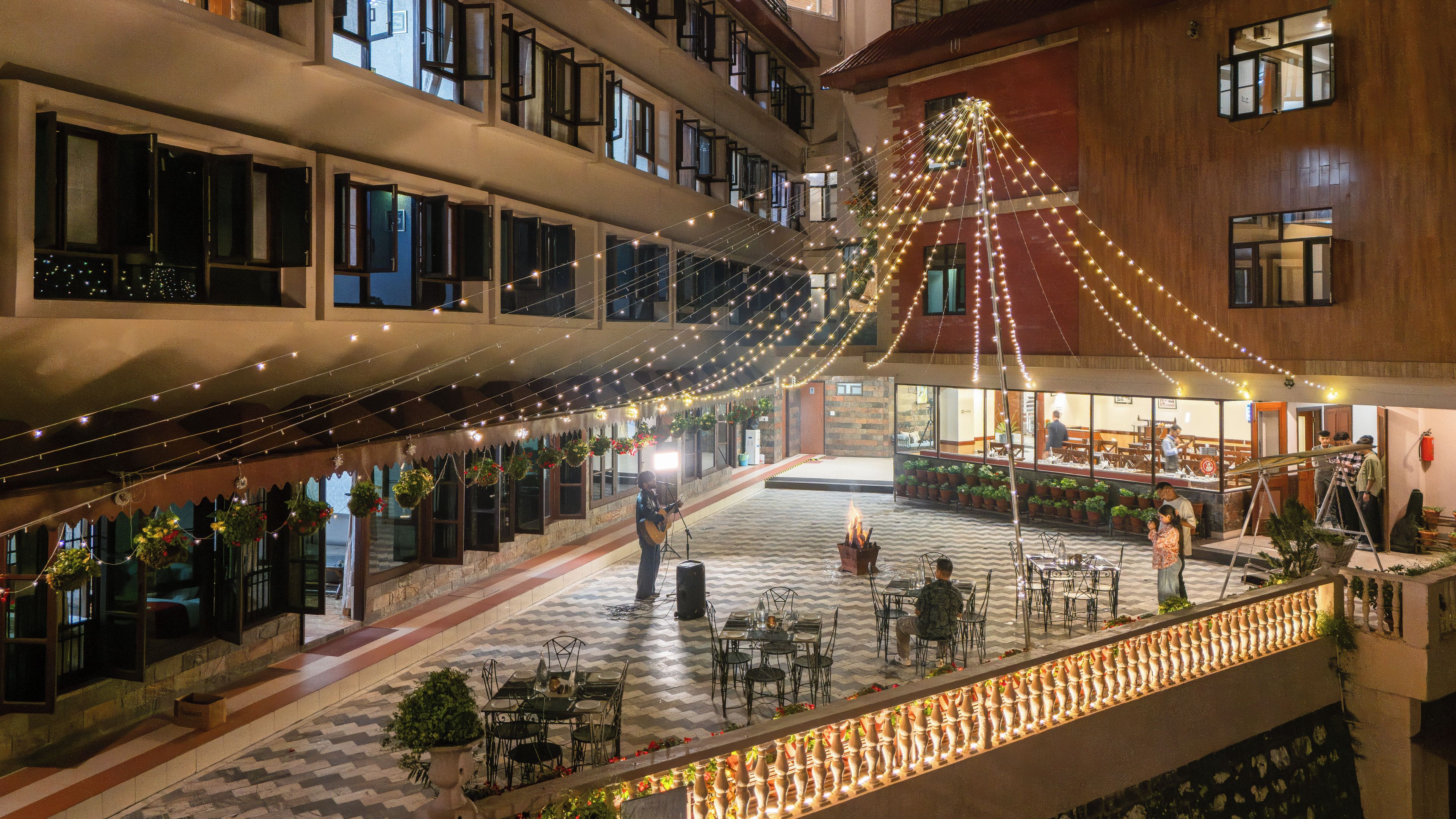 Un atrium d’hôtel à plusieurs niveaux, agrémenté de guirlandes lumineuses, de sièges en plein air et de plantes en pot.