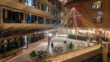 Un hall d'hotel de diversos nivells amb llums lluminoses, seients a l'aire lliure i plantes en testos.