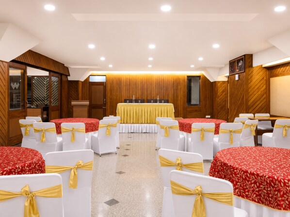 Une salle de conférence avec des chaises et des tables blanches, un lambris en bois et des spots encastrés au plafond.
