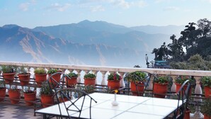 Una terraza con mesa y sillas, rodeada de macetas con plantas, con vistas a un paisaje montañoso.