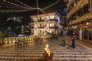 An outdoor dining area with tables and chairs, a fire pit, and string lights. - Hotel Vishnu Palace (Uttarakhand)