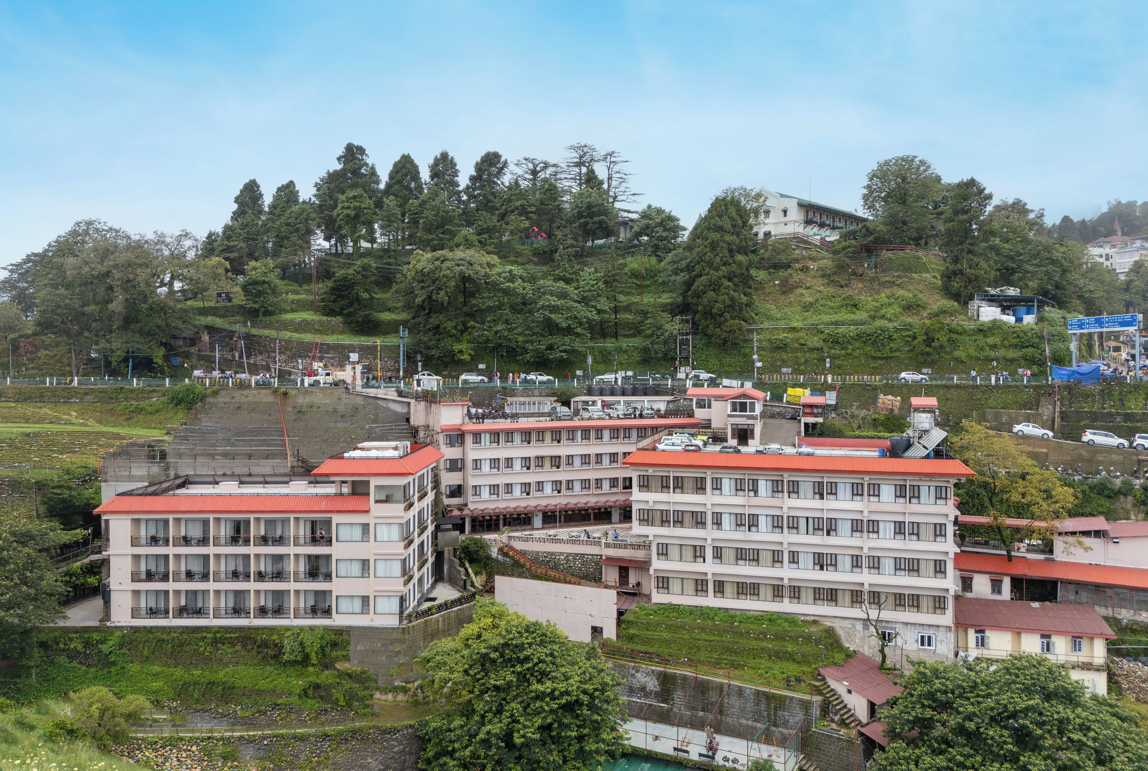 A multi-story hotel with a red roof, located on a hillside with a view of a river and surrounding greenery.