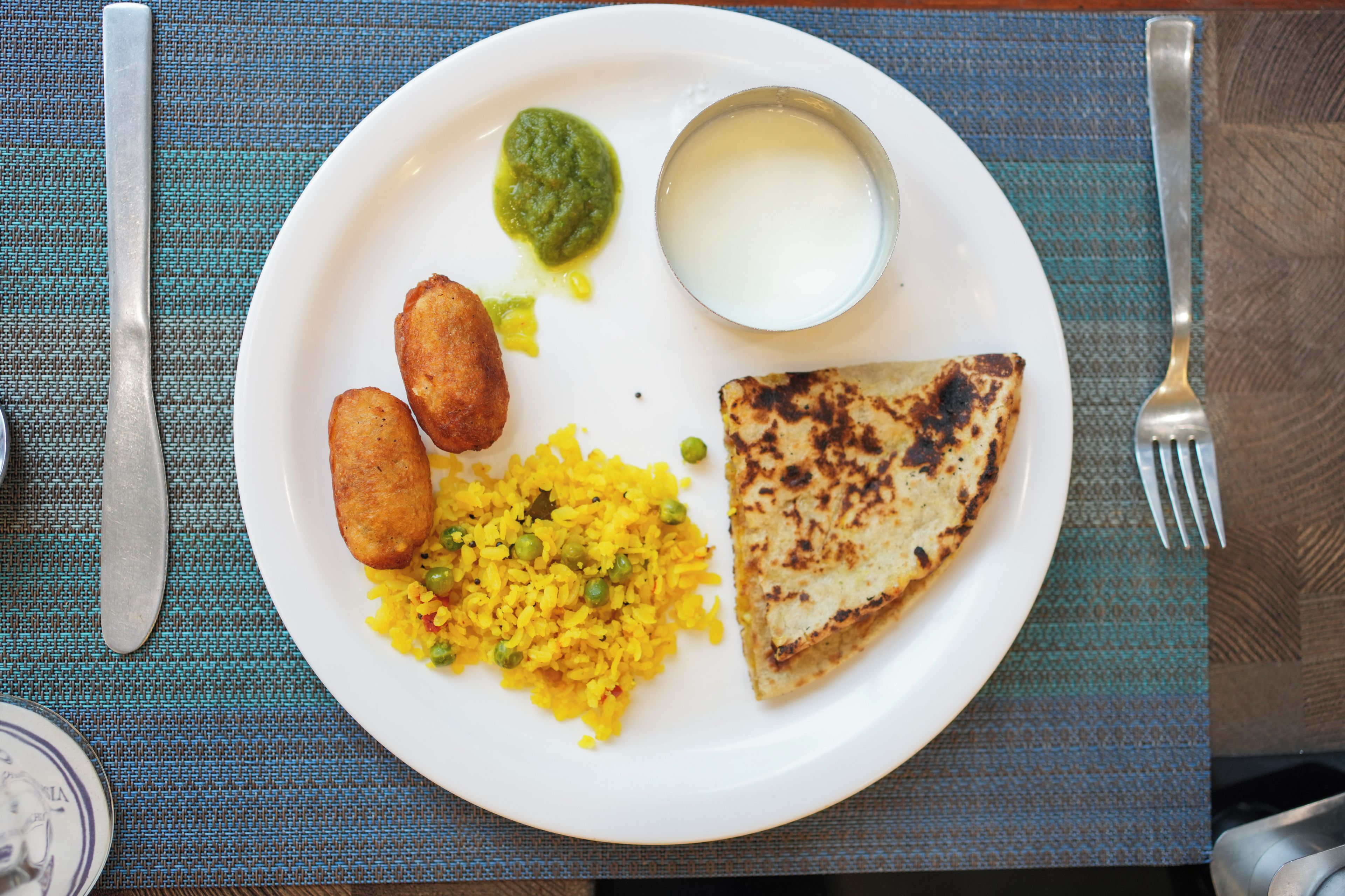 A plate with yellow rice, green peas, a piece of grilled bread, two fried items, and a bowl of green chutney.