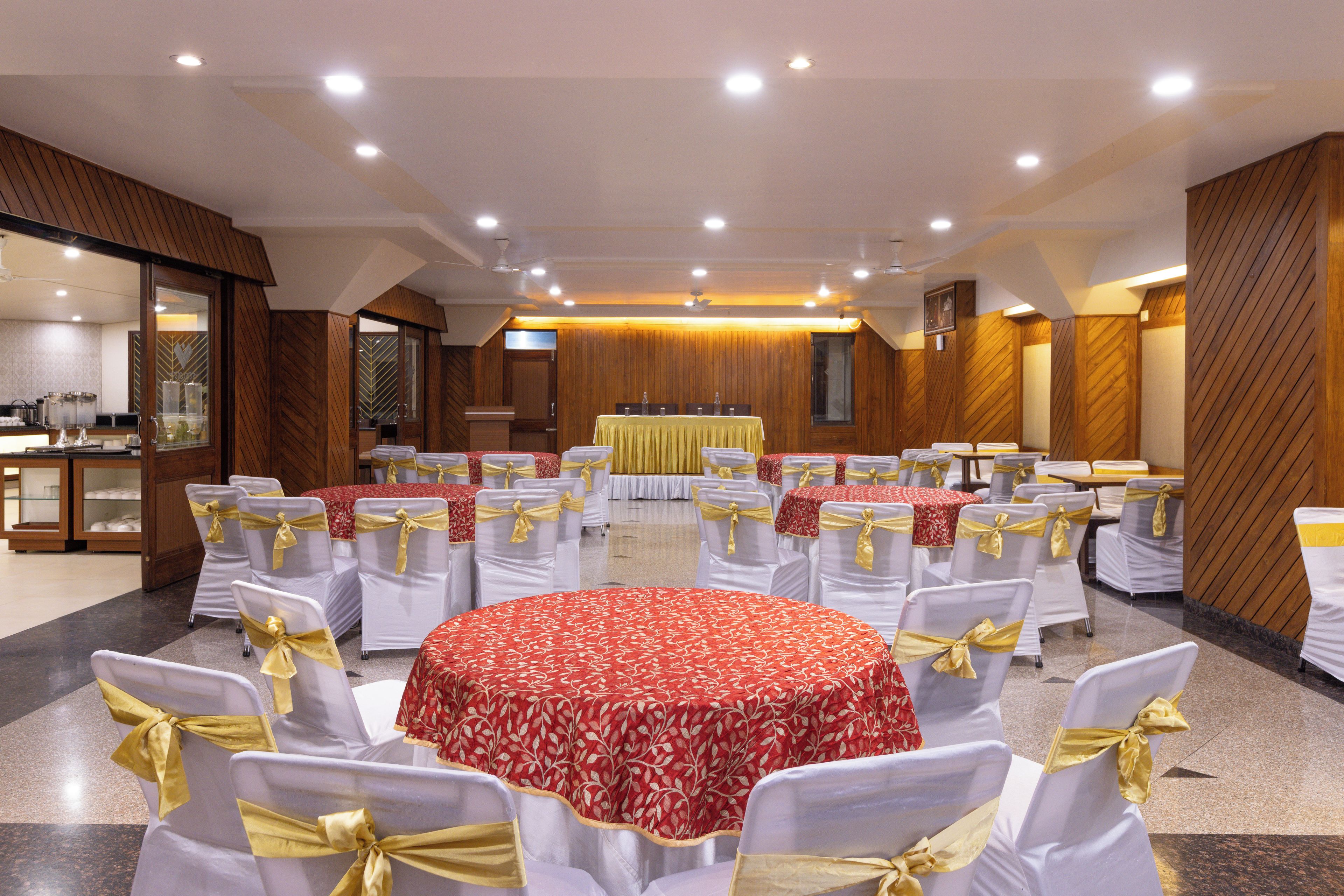 A banquet hall with round tables covered in red tablecloths, white chairs with gold sashes, and wooden paneling on the walls.