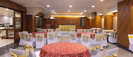 A banquet hall with round tables covered in red tablecloths, white chairs with gold sashes, and wooden paneling on the walls.