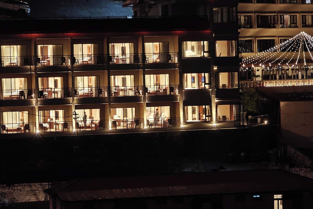 A multi-story hotel with balconies, a rooftop terrace, and string lights.