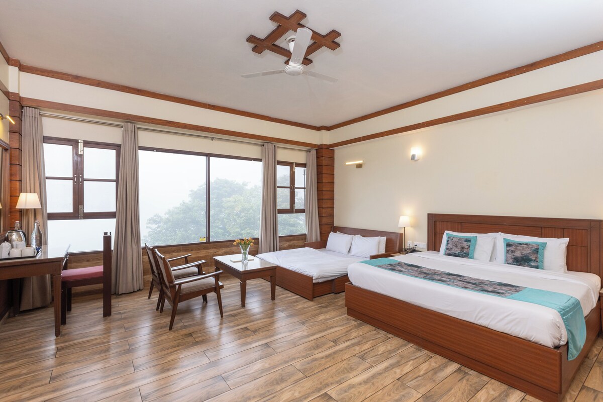 A hotel room with a wooden floor, a bed with white bedding, a desk with a chair, and a window with curtains.