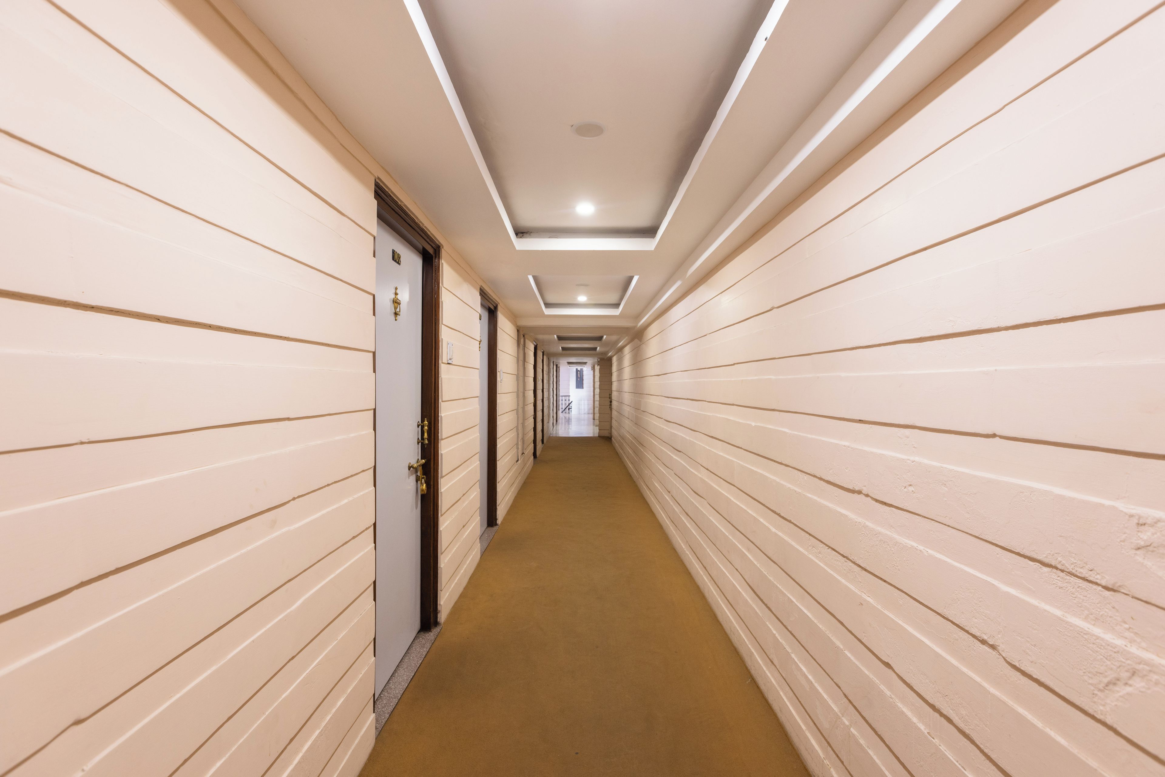 A long, narrow hallway with doors on both sides, a carpeted floor, and recessed lighting on the ceiling.