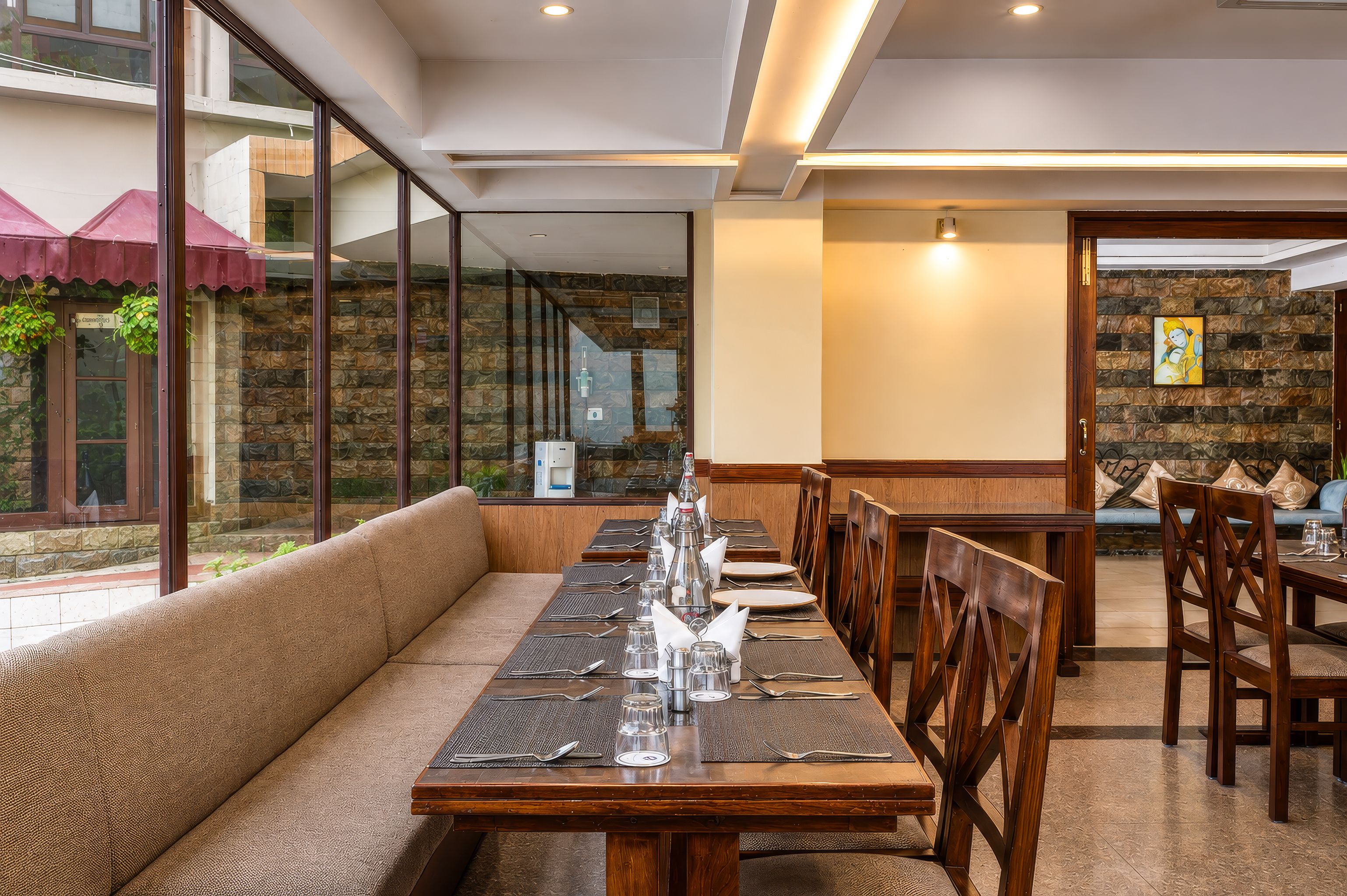 A restaurant with a long wooden table set for dining, a cushioned bench, and a stone wall.