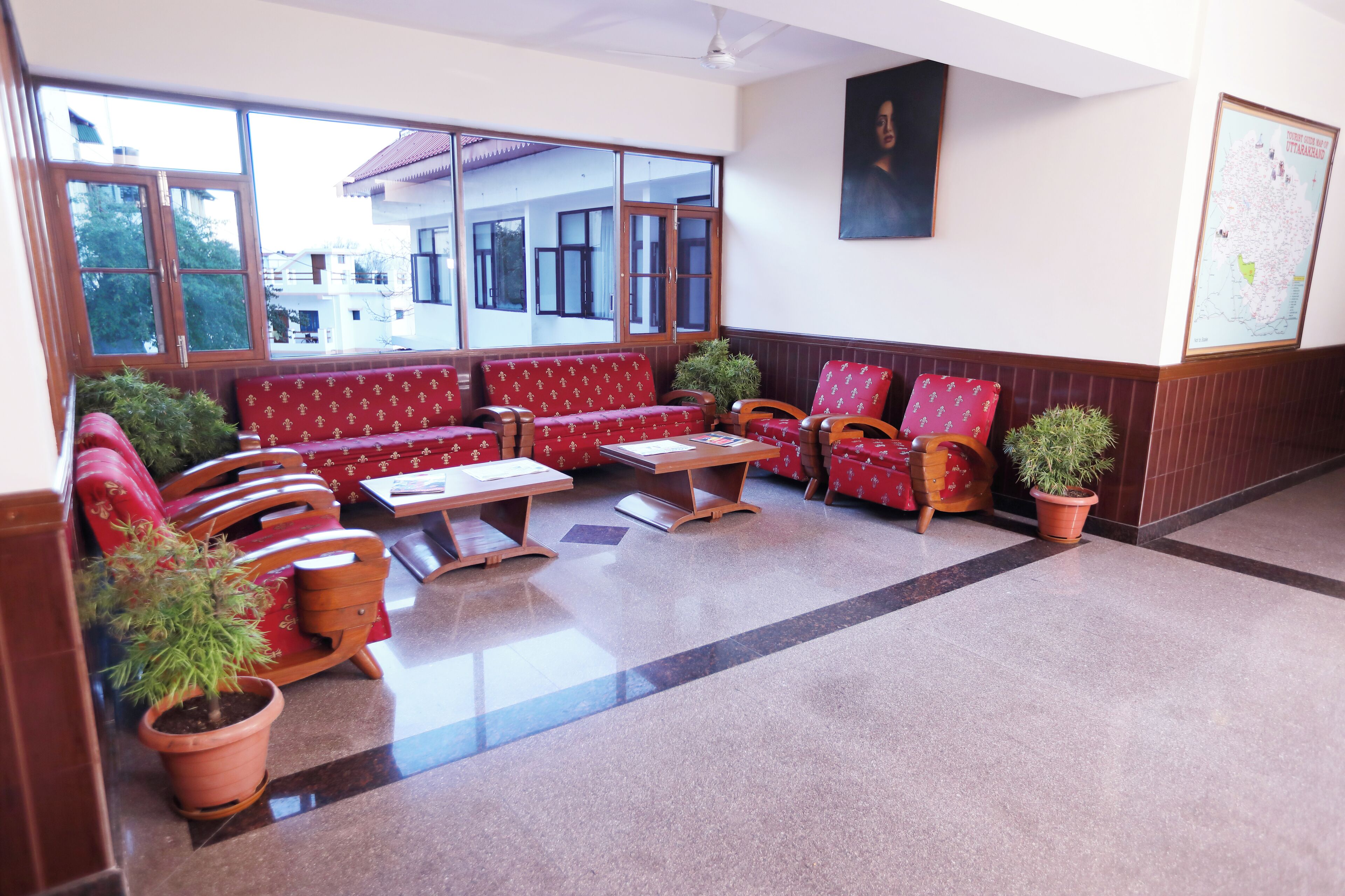 A lobby with red patterned sofas, wooden chairs, a coffee table, and potted plants.