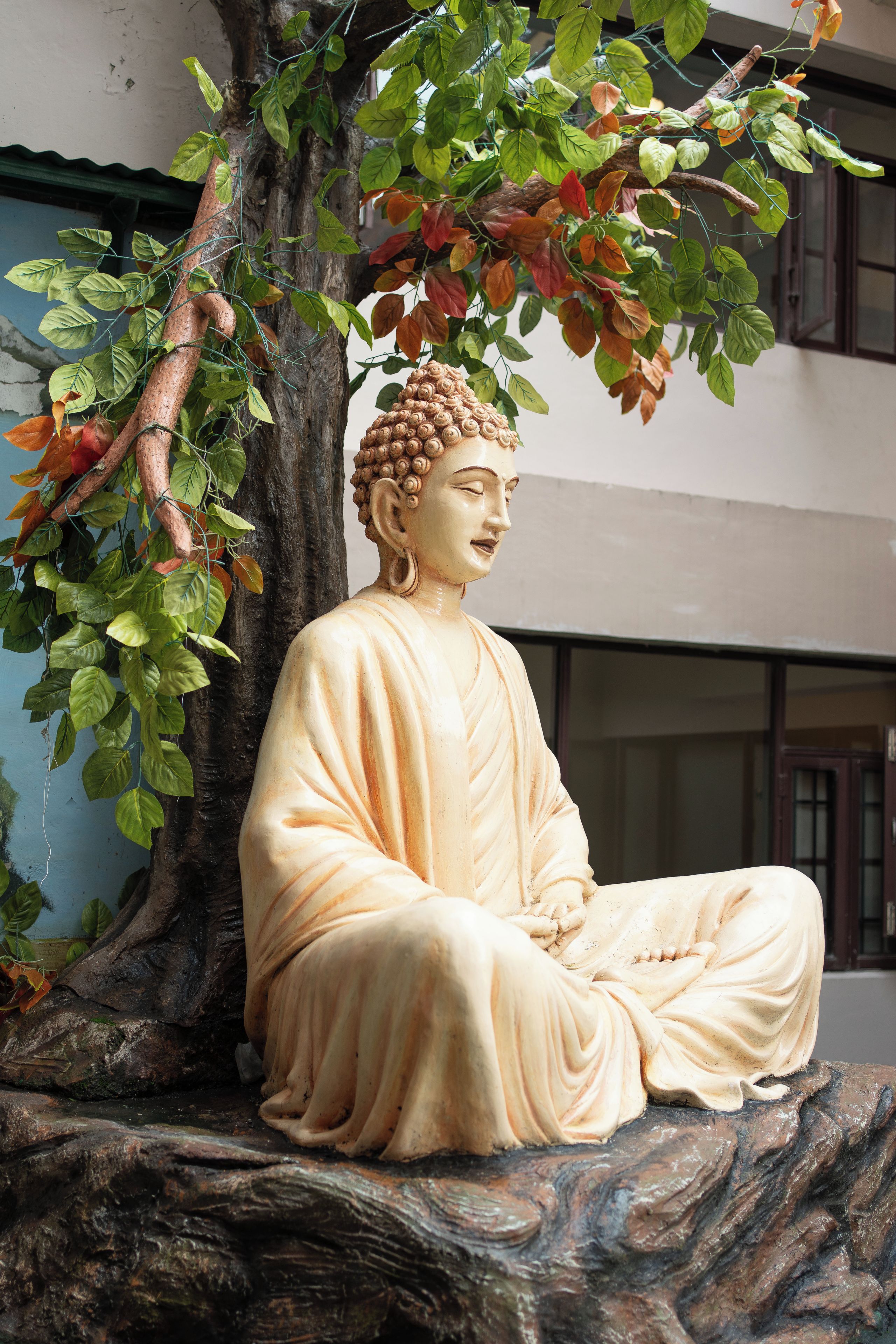 A statue of a seated figure with a tree and foliage in the background.