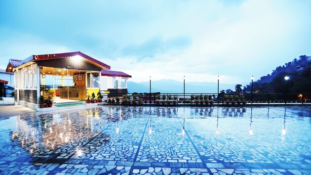 Un hotel con zona de piscina enlosada y vistas a la montaña.