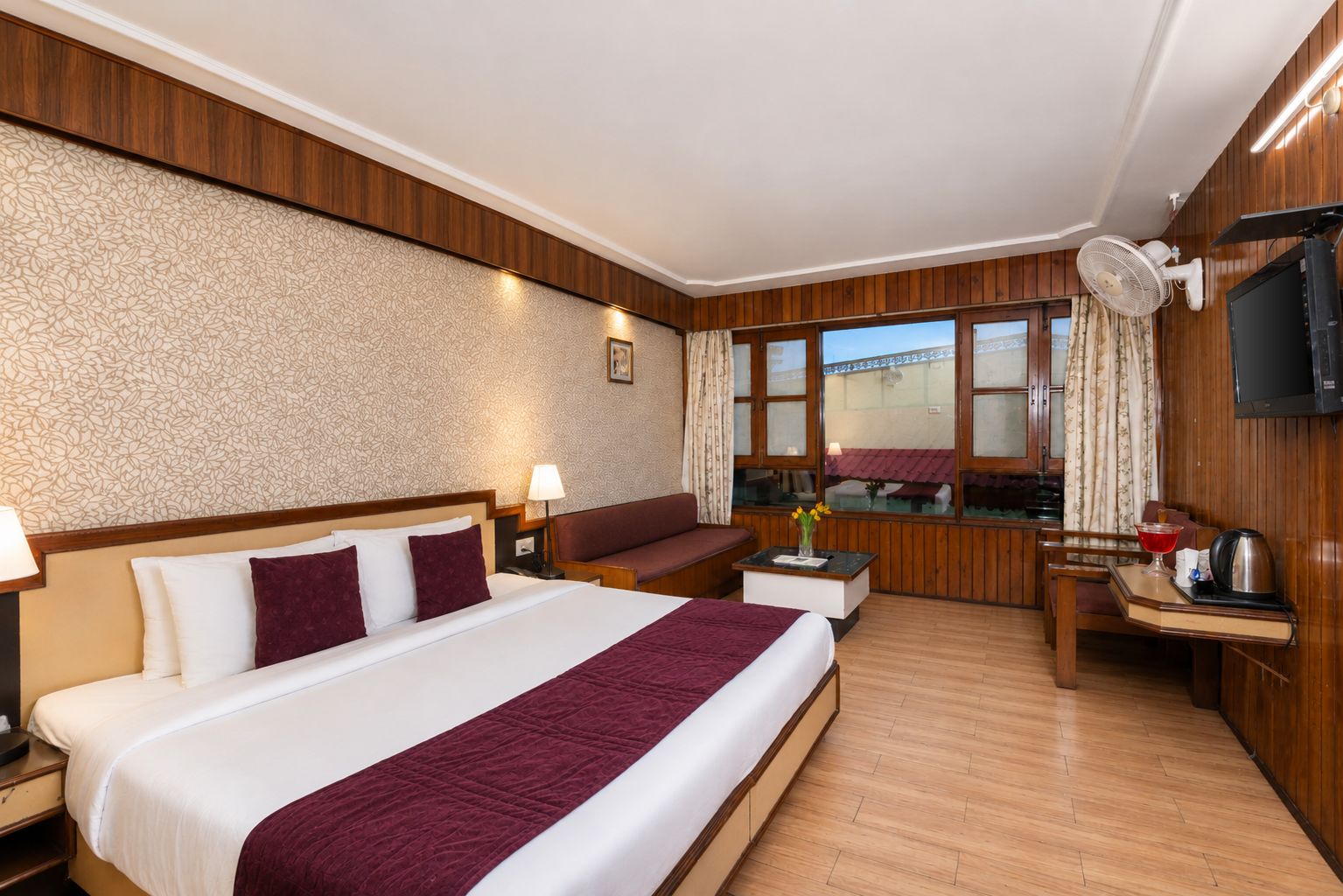 Ein Hotelzimmer mit einem großen Bett, einem Sofa, einem Schreibtisch mit Stuhl, einem Fernseher und einem Fenster mit Vorhängen.