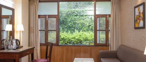 Una habitación con suelo de madera, un sofá marrón, una mesa de madera, una silla y un ventanal con vistas a zonas verdes.
