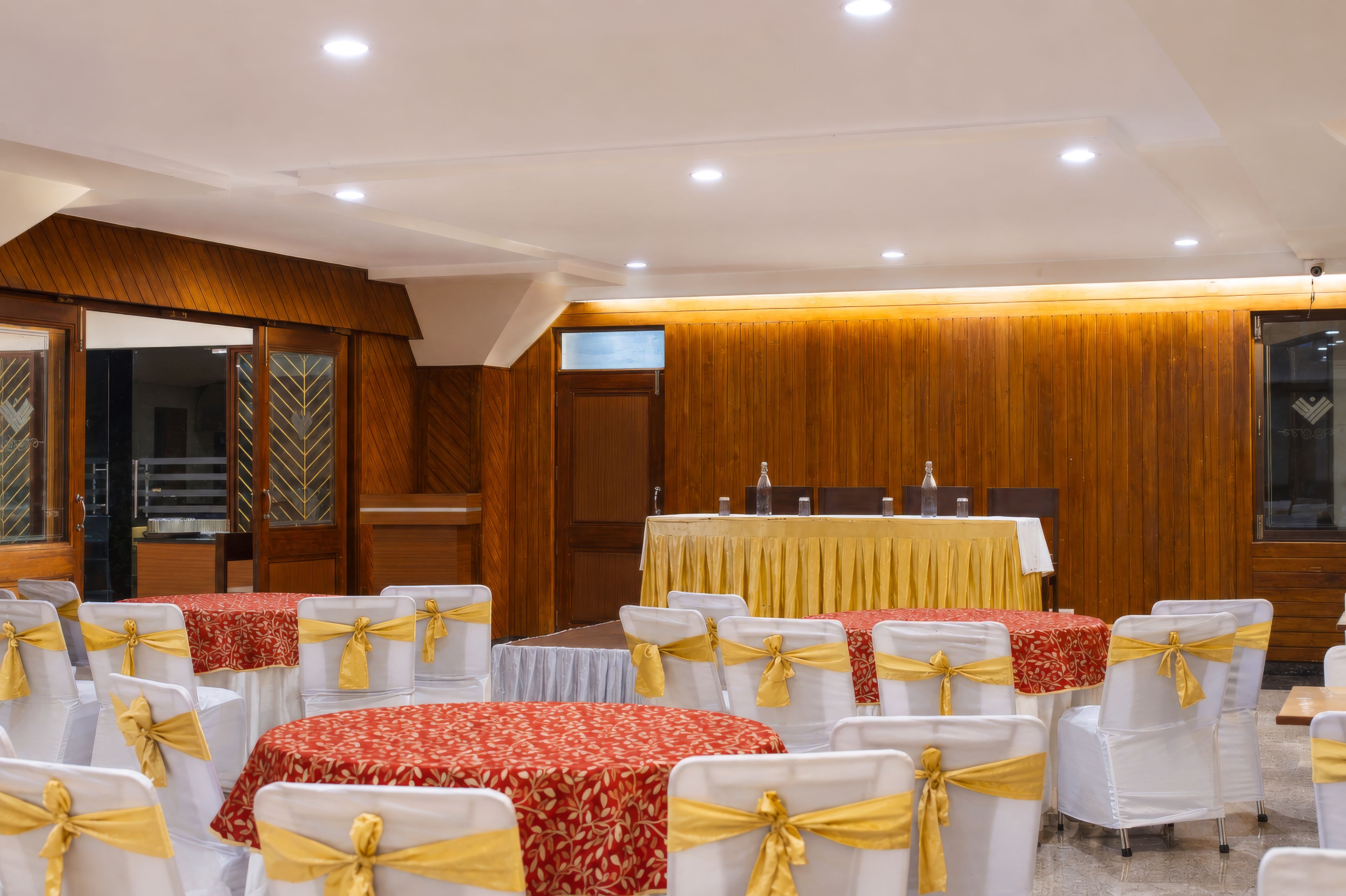 Un salón de conferencias con filas de mesas y sillas, paneles de madera en las paredes y una pantalla de televisión.