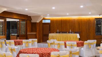 Un salón de conferencias con filas de mesas y sillas, paneles de madera en las paredes y una pantalla de televisión.