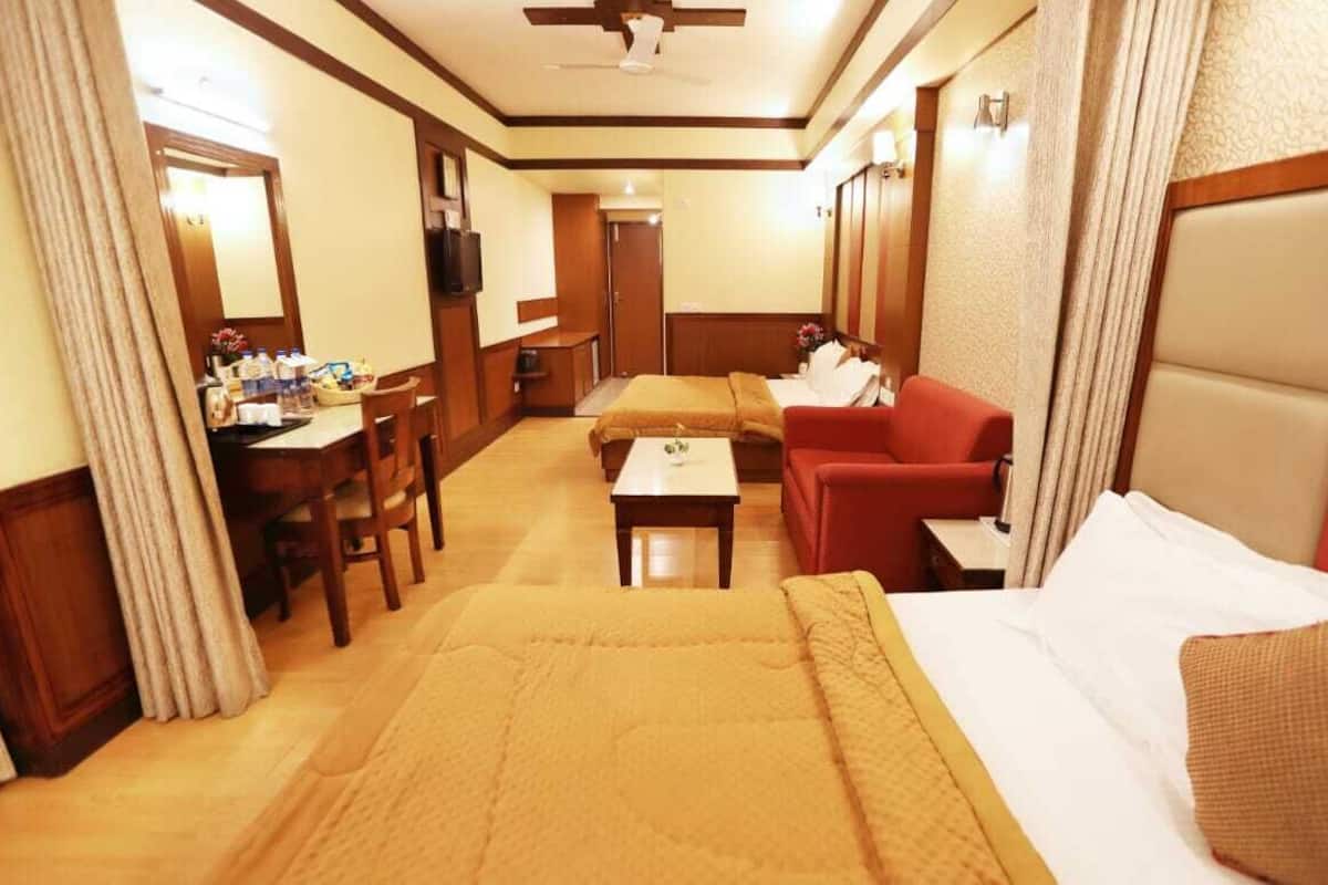 A hotel room with a bed, a red sofa, a small table, a desk with a chair, and a television.