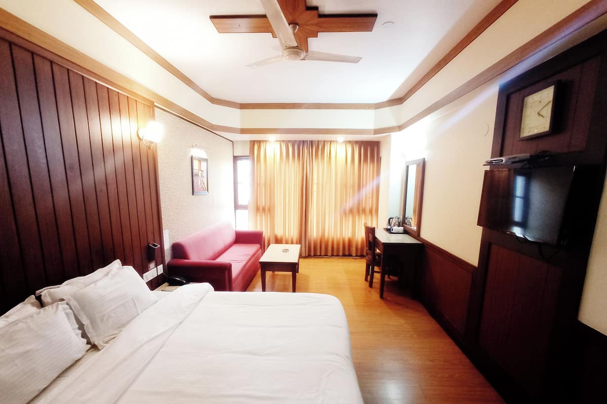 A hotel room with a large bed, a red sofa, a desk with a chair, a television, and a ceiling fan.